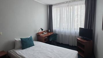 Una habitación de hotel con cama, escritorio, silla, televisor y ventana con cortinas.