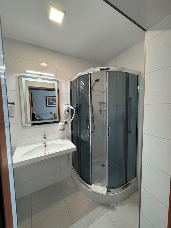Une salle de bain moderne avec une douche à parois de verre, un lavabo blanc et un miroir au-dessus du lavabo.