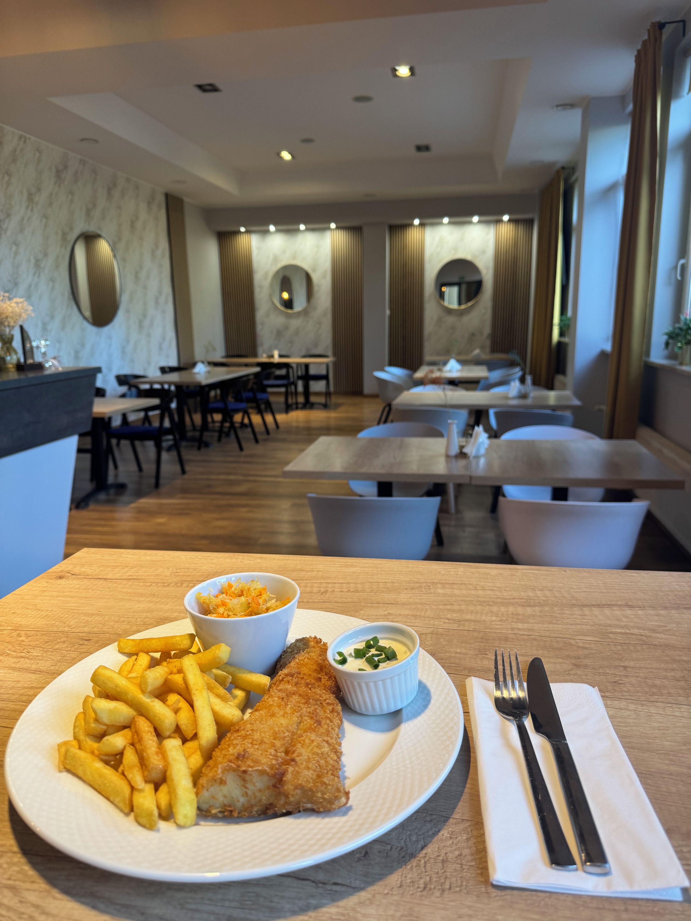 A dining area with tables, chairs, and a plate of food including fries and a breaded item, with a mirror and wall decor.