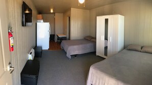 Habitación con dos camas, un escritorio, un armario, un extintor y un televisor en la pared.