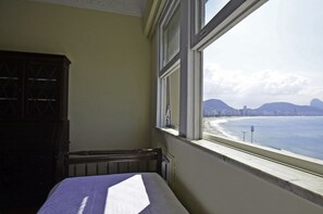A room with a bed, a window overlooking a beach, and a radiator.