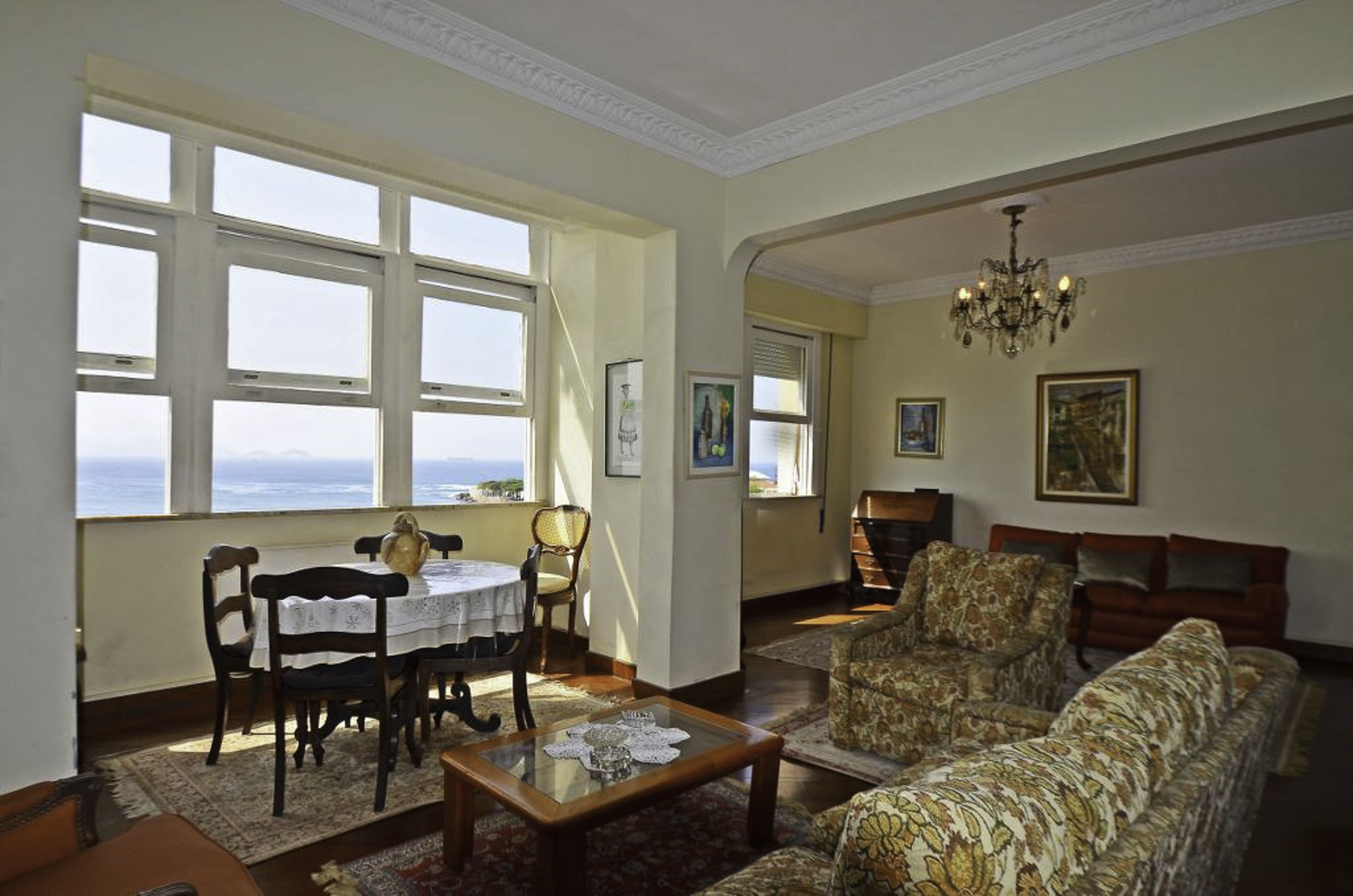 A living room with a dining area, large windows, a chandelier, and patterned furniture.