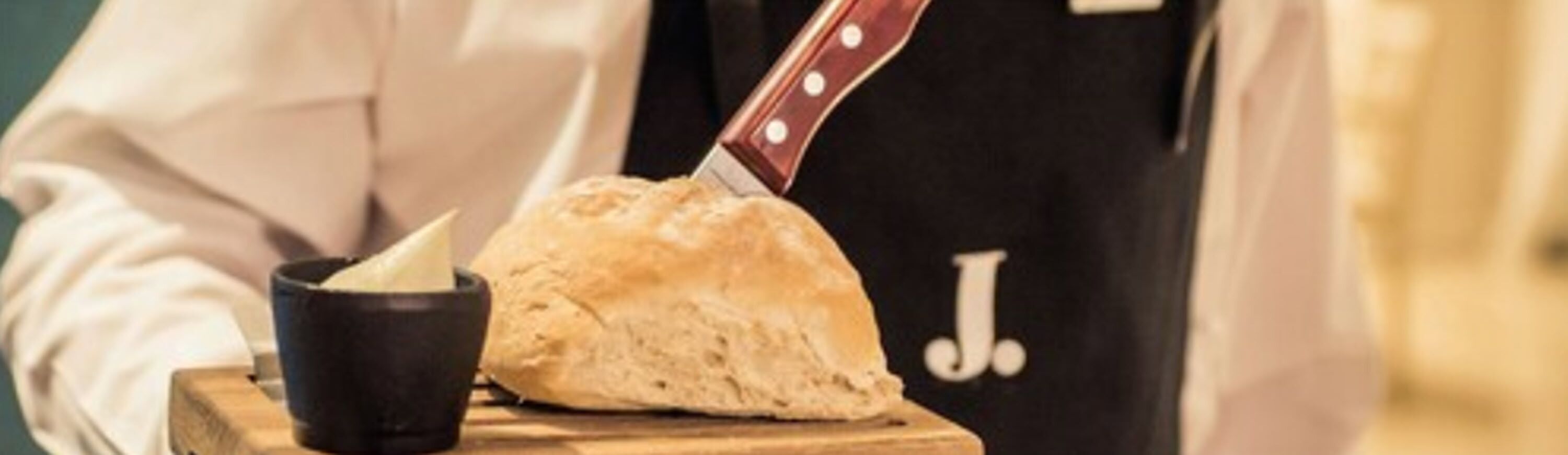A loaf of bread on a wooden board with a knife and a black cup beside it.