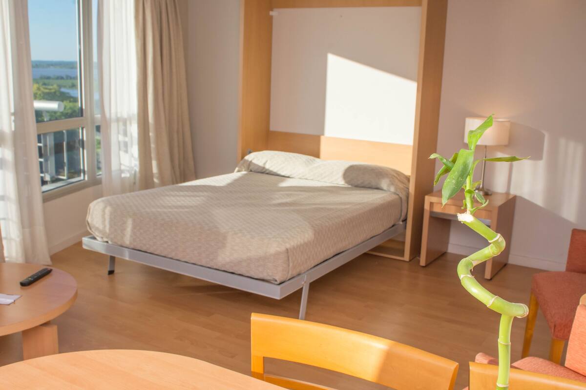 Une chambre d’hôtel moderne équipée d’un lit, d’un bureau, d’une chaise, d’une lampe et offrant une vue sur l’extérieur.