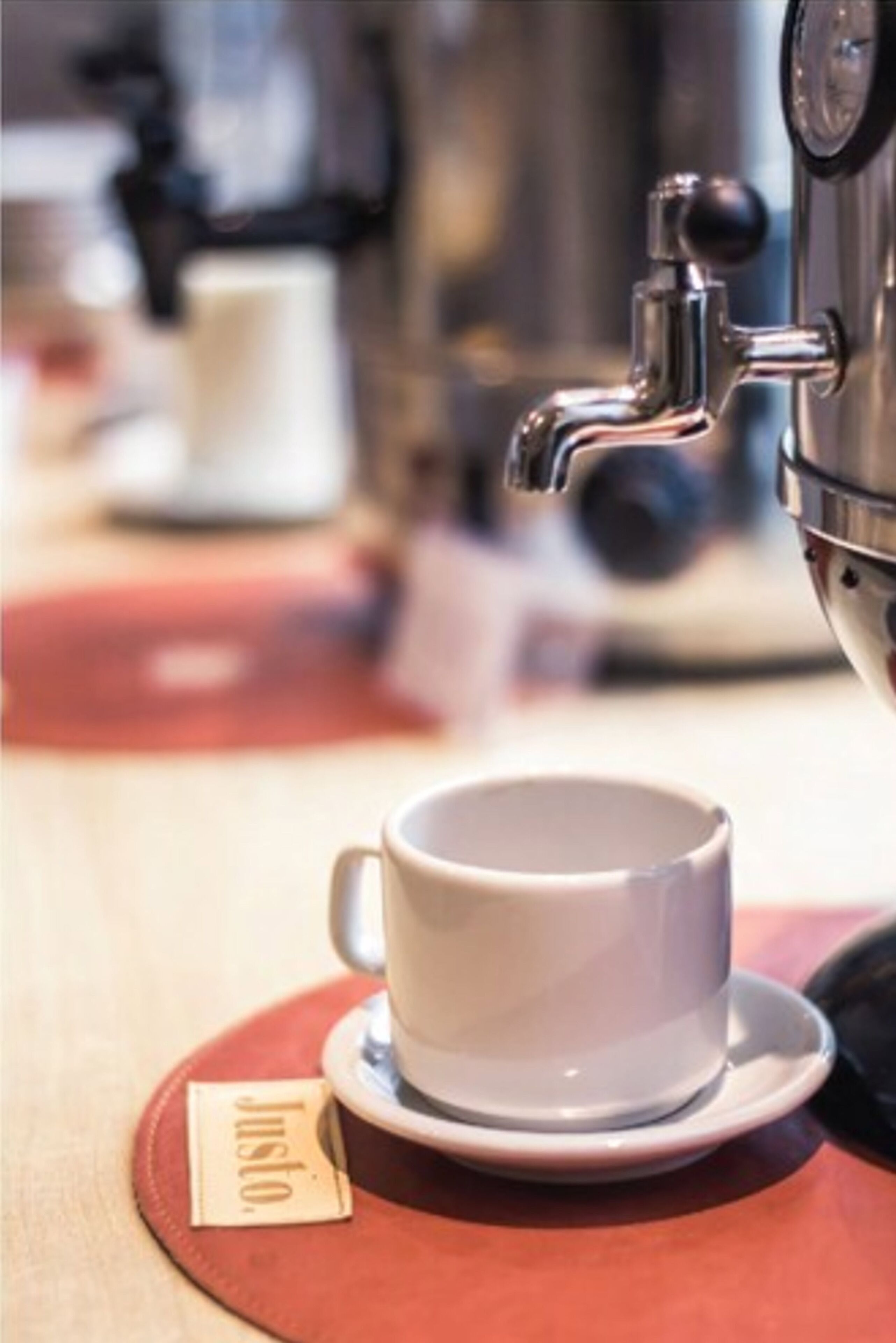 Una cafetera con una taza y un platillo sobre un posavasos rojo.