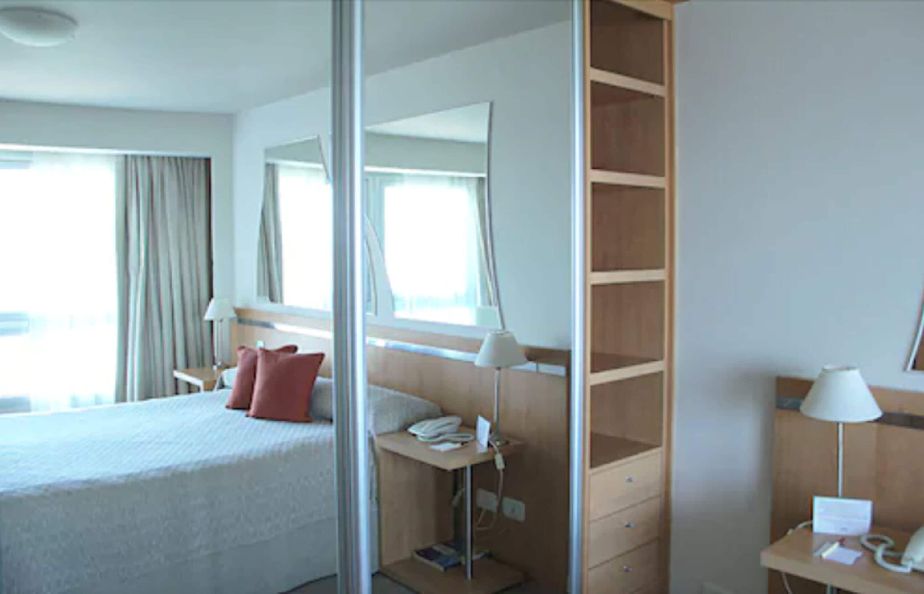 Una camera d'albergo con un letto, comodini, una scrivania, una lampada e uno specchio.