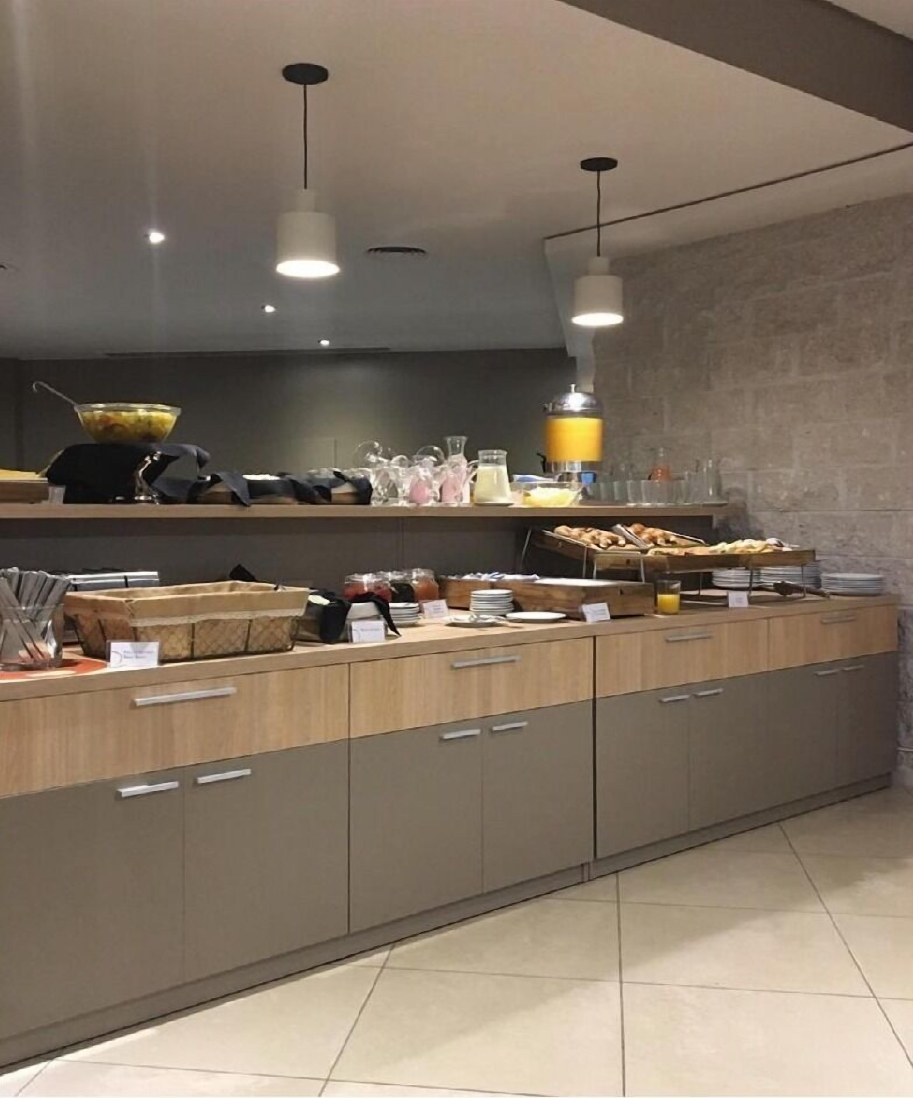 A modern kitchen with a long counter, overhead lighting, and various kitchen appliances.