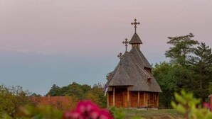 Una iglesia de madera con techo de paja y cruces en la parte superior, rodeada de vegetación.
