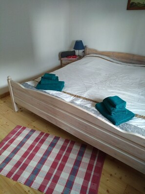 A bed with a wooden frame, a white mattress, and two folded towels. A checkered rug is on the floor. - Ferienhaus Burkard (Epenwöhrden)