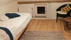 A small, cozy room with a single bed, a chair, a radiator, and a window.