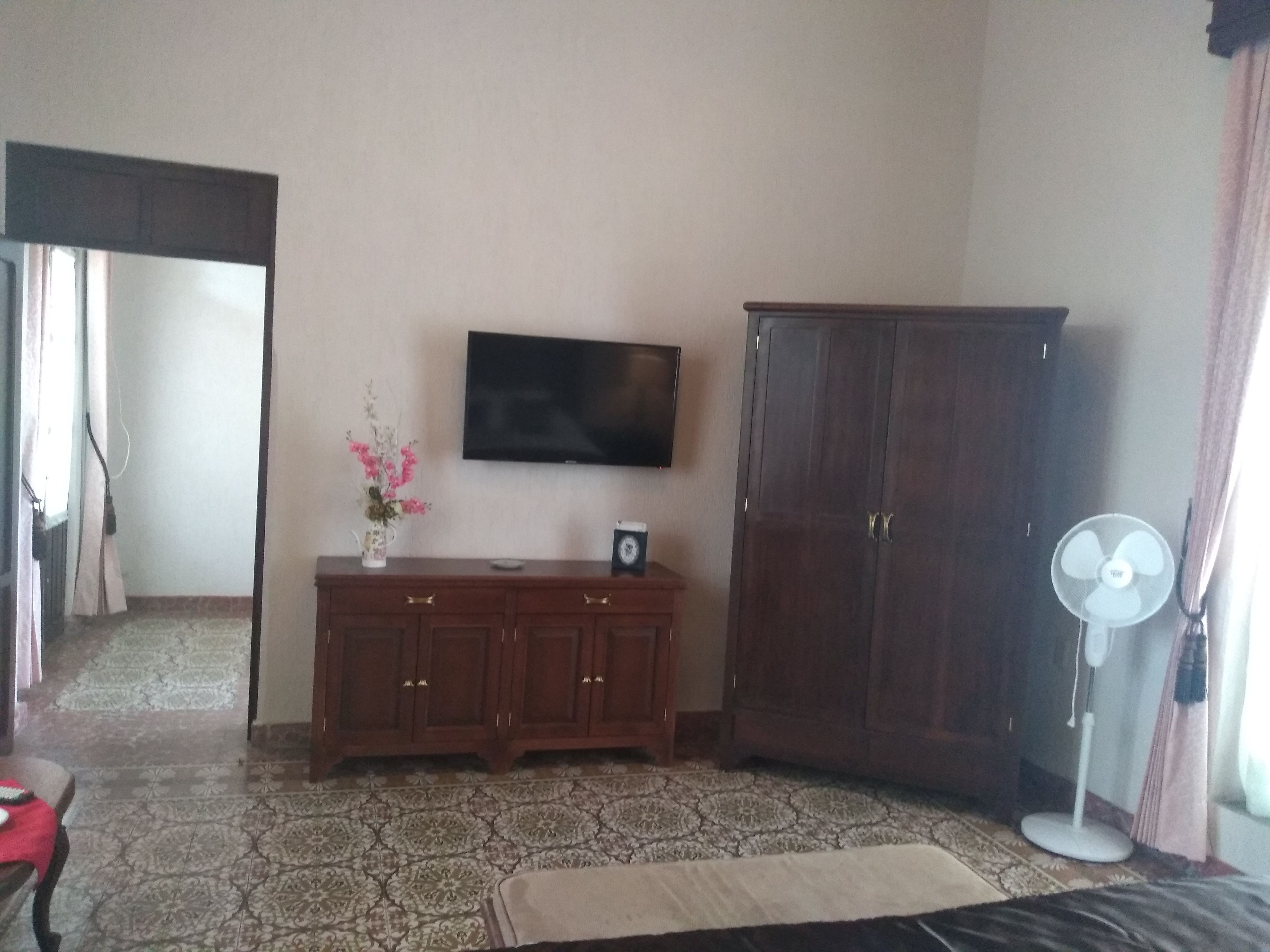 A room with a TV on the wall, a wooden cabinet, a fan, and patterned flooring.