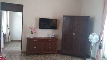 A room with a TV on the wall, a wooden cabinet, a fan, and patterned flooring.