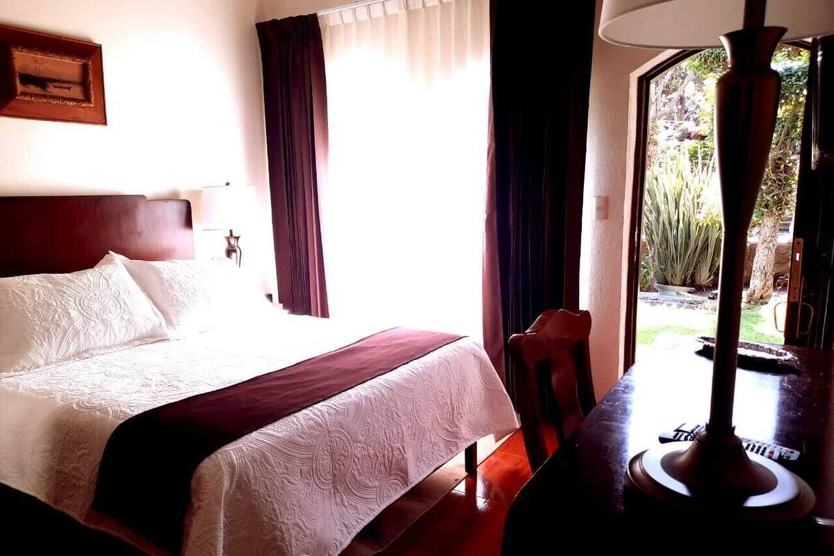 Een hotelkamer met een bed, een stoel, een lamp en een raam met gordijnen.