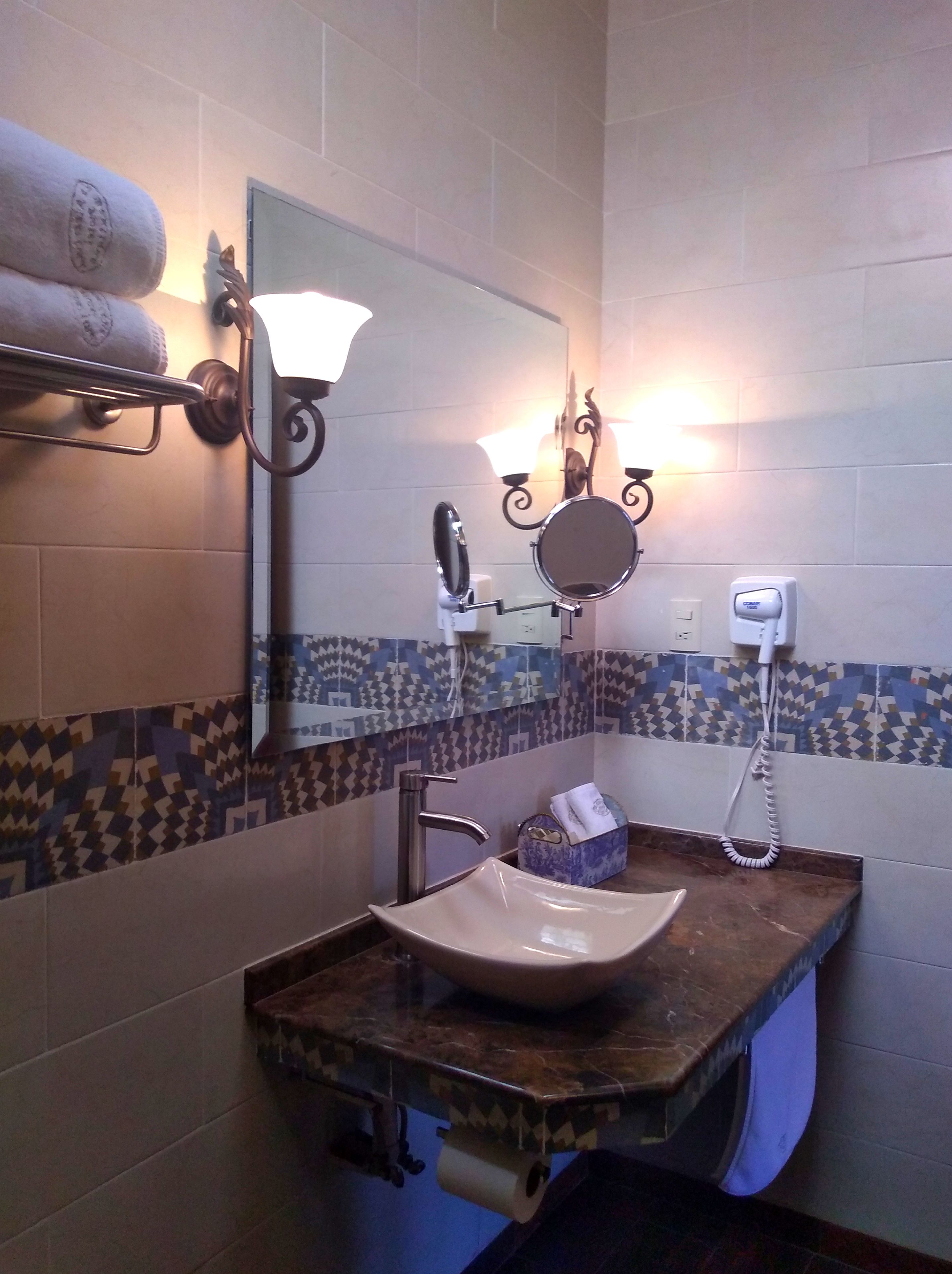 A bathroom with a marble sink, a towel rack with towels, a mirror, a wall-mounted light fixture, and a hand dryer.