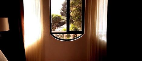 Un dormitorio con cama, ventana con vistas a la vegetación y cortinas.