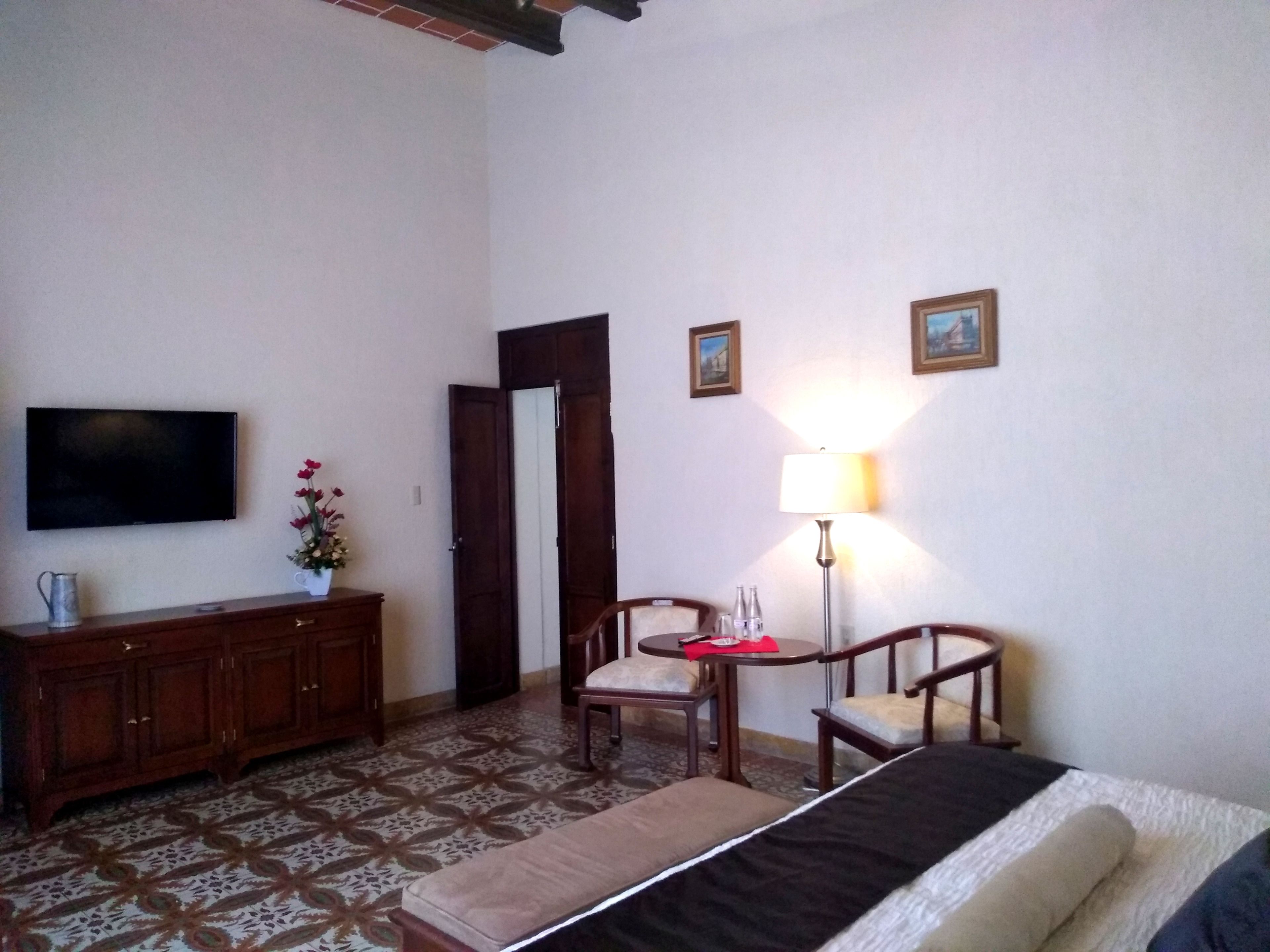 Una habitación de hotel con cama, televisor, escritorio con silla, lámpara y armario.