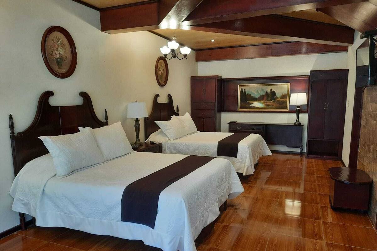 Een hotelkamer met twee bedden, houten vloeren, een schilderij aan de muur en een kroonluchter.