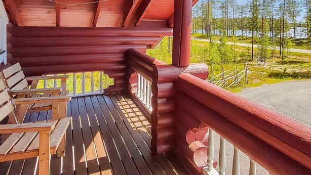 A wooden deck with benches, a railing, and a view of a forest and water. - Harjurinne by Interhome (Lestijärvi)