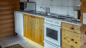 A compact kitchen with wooden cabinets, a microwave, a stove, and a sink. - Harjurinne by Interhome (Lestijärvi)
