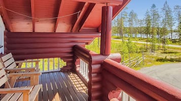 A wooden deck with a red railing, overlooking a forest and a road.