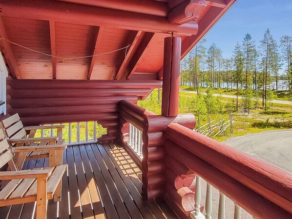 A wooden deck with a red railing, overlooking a forest and a road.
