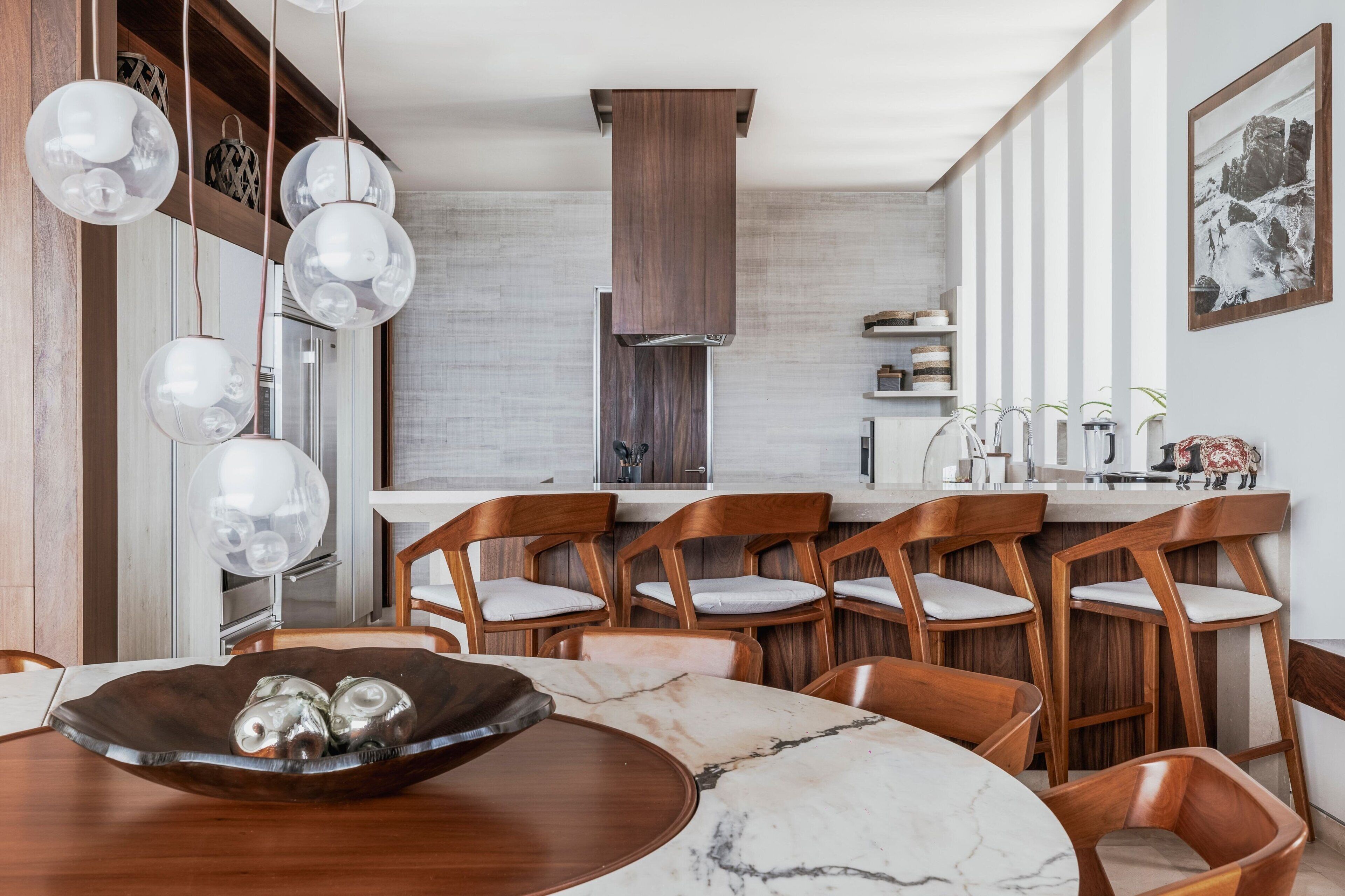 A modern kitchen with wooden chairs, a marble table, and pendant lights.