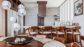 A modern kitchen with wooden chairs, a marble table, and pendant lights.