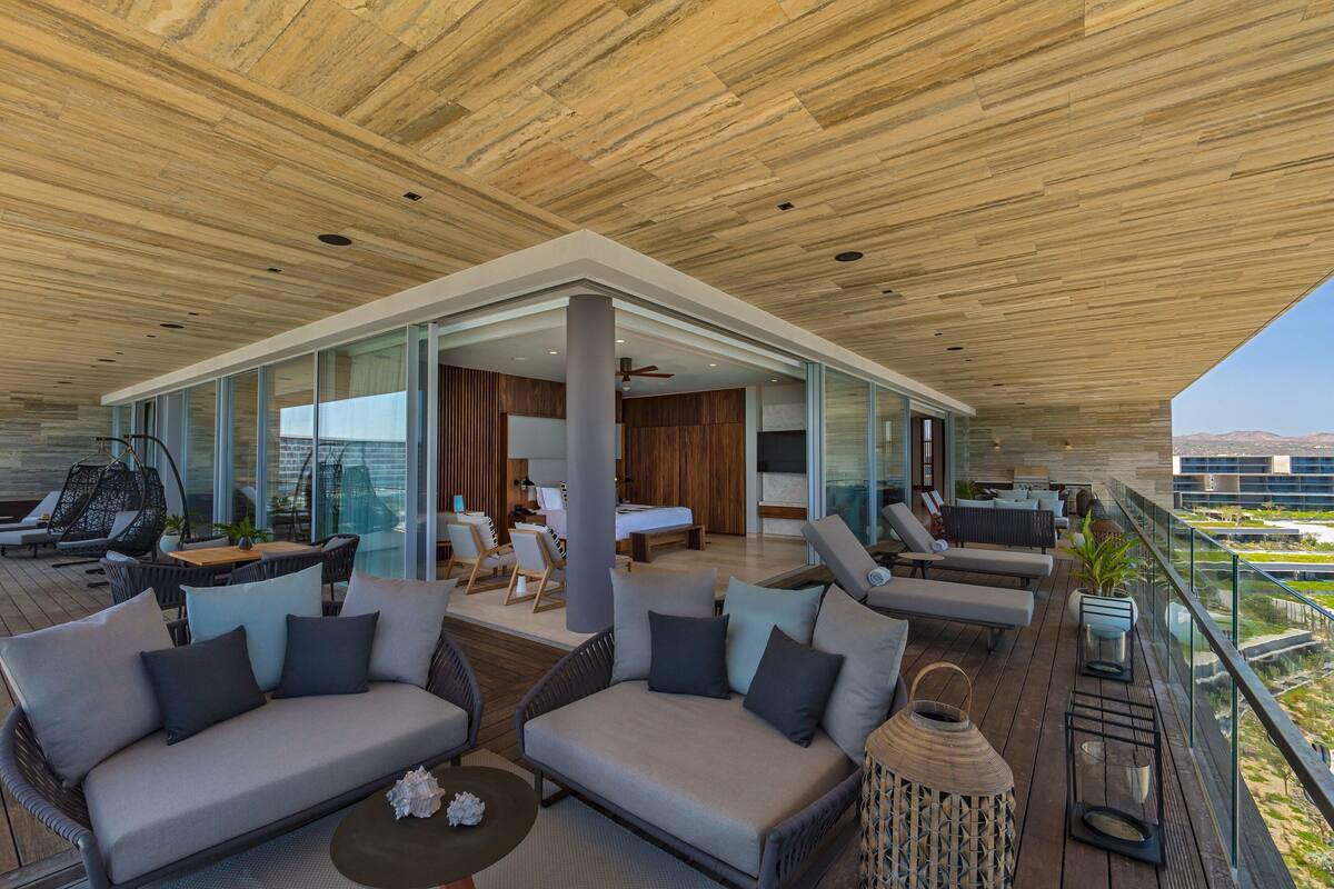 A modern outdoor living area with a wooden ceiling, glass walls, and a balcony overlooking a cityscape.
