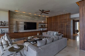 A modern living room with a large flat-screen TV, a ceiling fan, and a wooden partition.