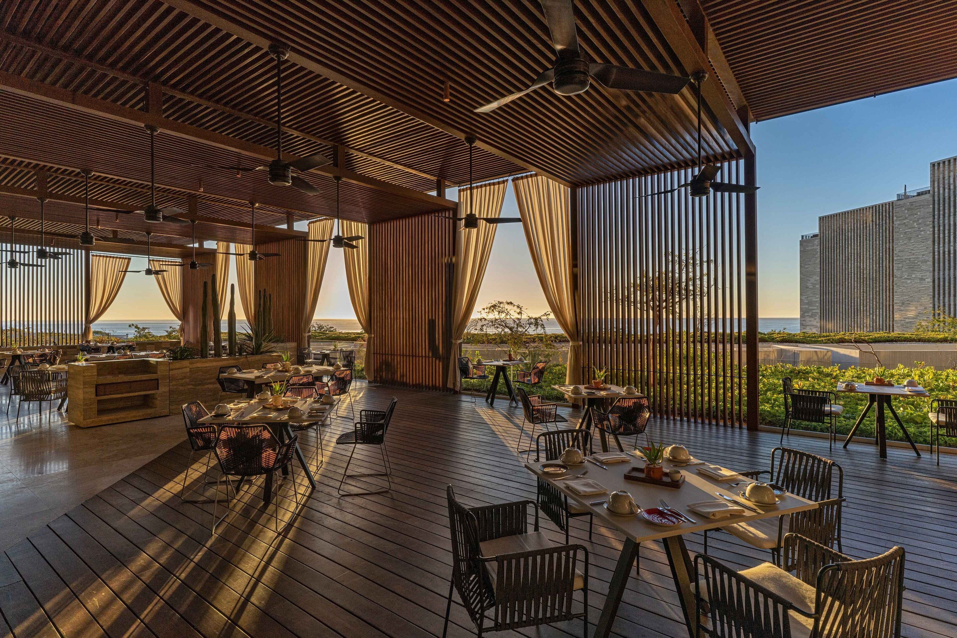 Un espacio de comedor al aire libre con piso de madera, mesas y sillas, con vista a un paisaje pintoresco.