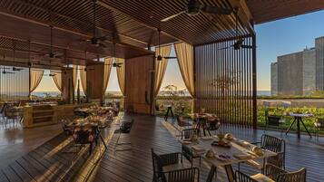 Un espacio de comedor al aire libre con piso de madera, mesas y sillas, con vista a un paisaje pintoresco.