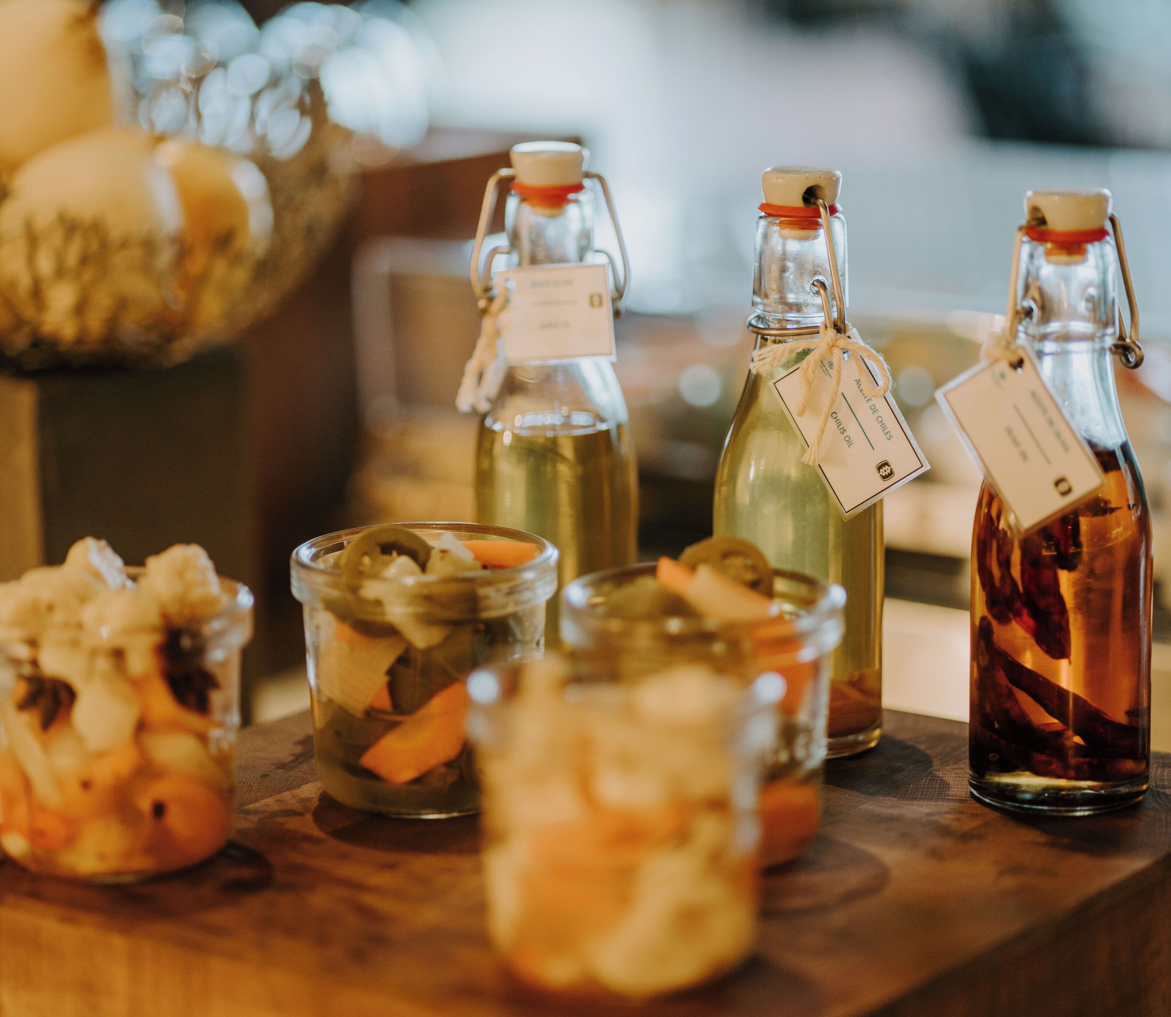 Variedad de recipientes de vidrio con etiquetas, probablemente conteniendo frutas conservadas o encurtidos, sobre una superficie de madera.