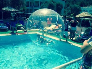 A transparent dome over a swimming pool with people inside and outside.