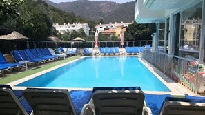 A swimming pool with blue lounge chairs and a view of buildings in the background. - Icmeler Prestij Apart (Marmaris)