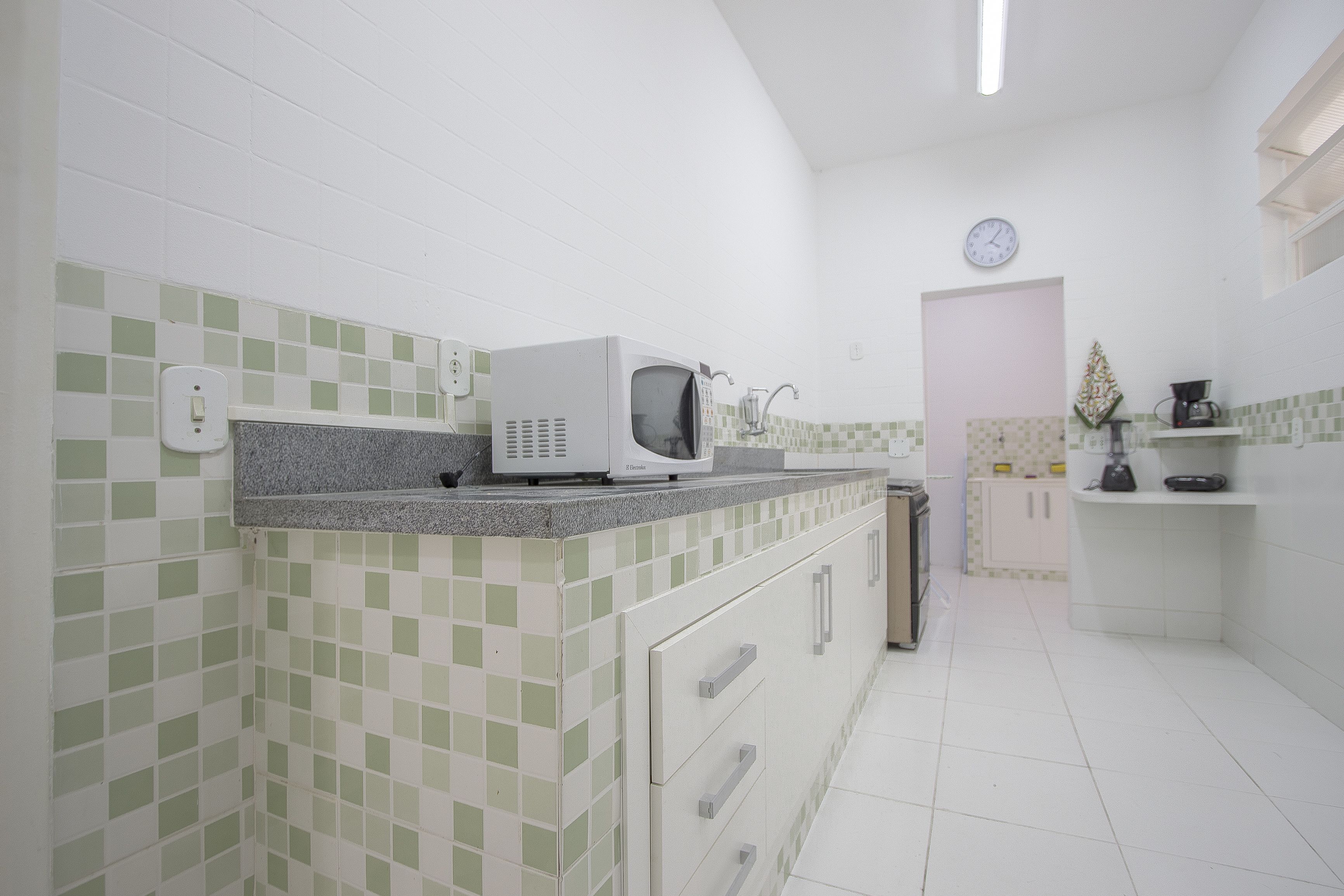 Une cuisine avec des meubles blancs, un four à micro-ondes et une horloge au mur.