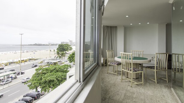 A balcony with a view of the beach, a dining table with chairs, and a cityscape in the background. - LineRio Vista Mar Copacabana 460 (Rio de Janeiro)