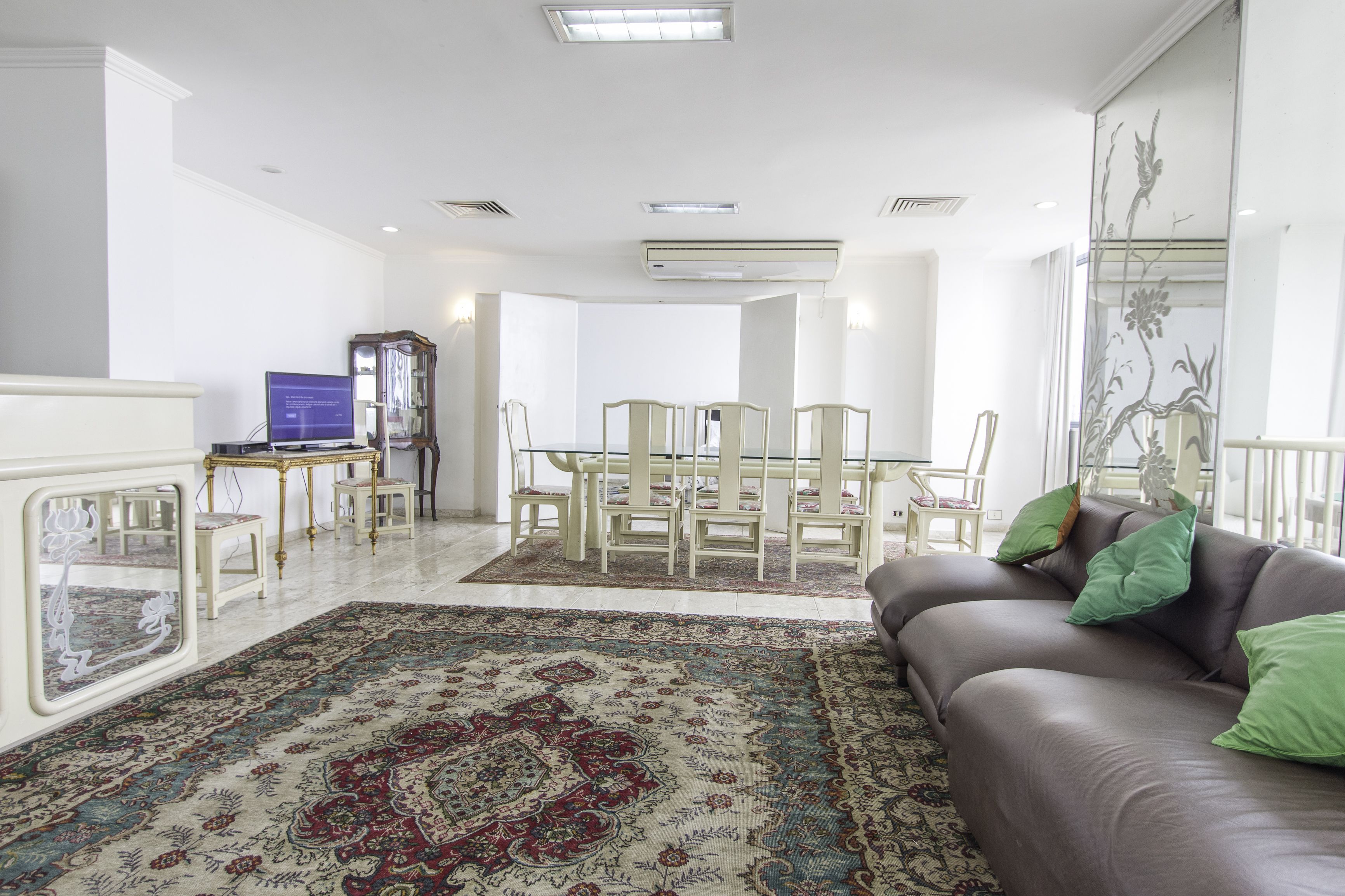 A spacious living room with a large sofa, a dining table with chairs, and a television.