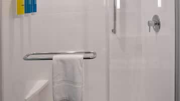 Ducha envuelta en cristal con pared de azulejos blancos, cabezal de ducha manual y toallero con una toalla blanca.