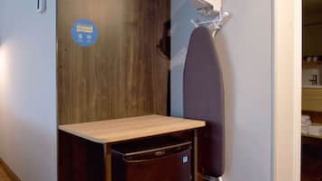A compact room with a wooden desk, a hanging clothes rack, and a wall-mounted ironing board.