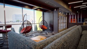 Un espacio lounge moderno con un sofá, dos sillones colgantes y vistas a un edificio.