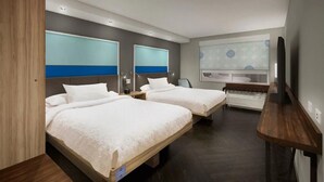 Habitación de hotel con dos camas, un espejo grande, televisión y baño con lavamanos y espejo.