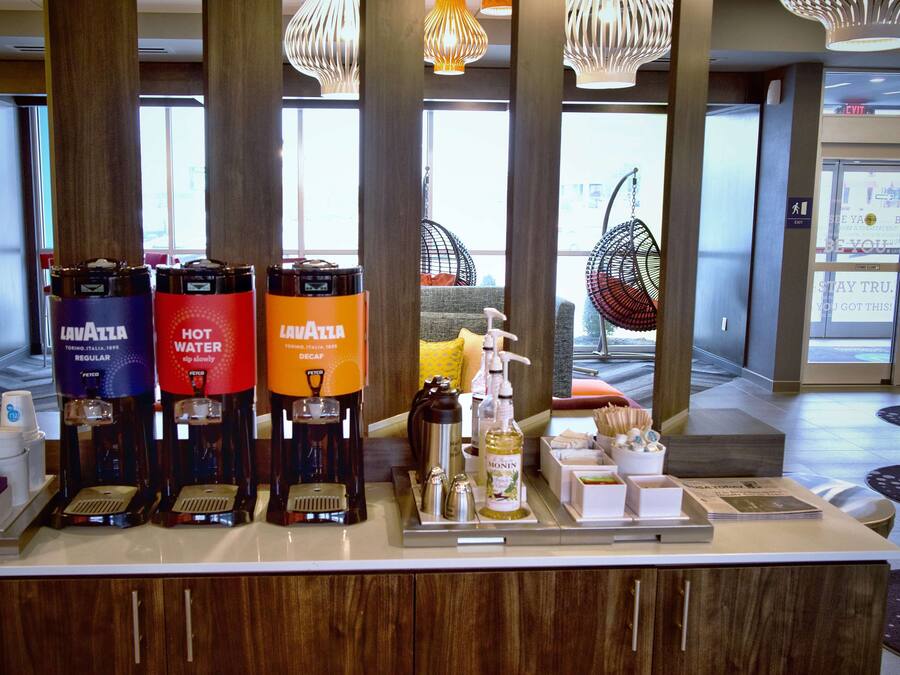 A coffee station with multiple beverage dispensers, a hand soap dispenser, and a tray with various items including a bottle of lotion and a magazine.