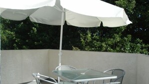 An outdoor patio with a glass table and metal chairs, covered by a white umbrella.