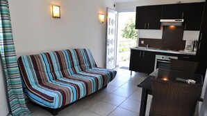 A modern living room with a striped sofa, a dining table with a chair, and a kitchen area with dark cabinets and a stove.