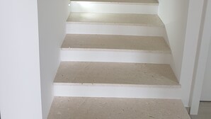 Een trap met witte muren en beige treden die uitkomen op een plateau.