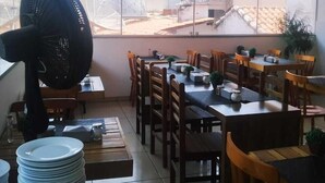 A dining area with tables and chairs, a large fan, and a view of buildings outside. - Capivari Centro Hotel (Capivari)