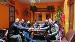 A group of people seated around a table in a room with orange walls, a fire extinguisher, and a small window. - International Hostels (Cusco)