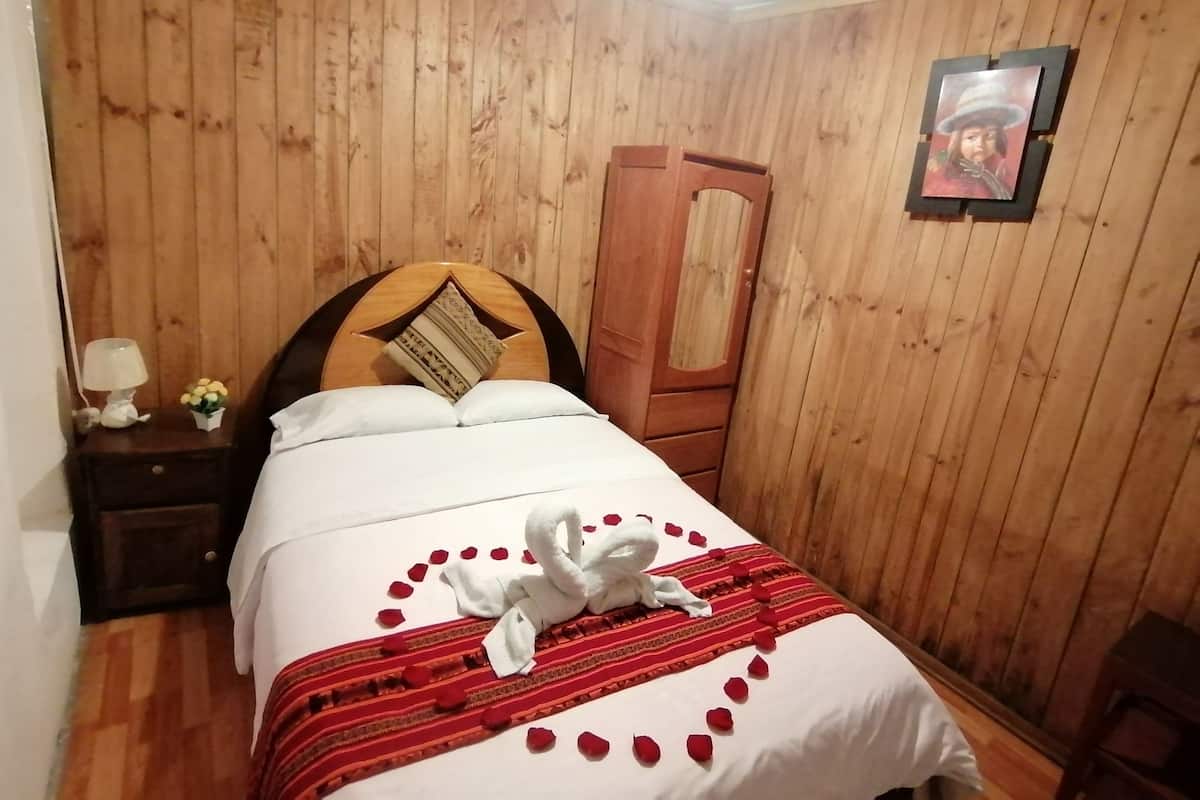 Ein Zimmer mit Holzwänden, einem Bett, einem Nachttisch, einer Lampe und einem gerahmten Bild an der Wand.