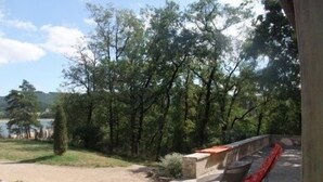 Un patio con pared de piedra, una silla reclinable roja y vista a un lago rodeado de árboles.