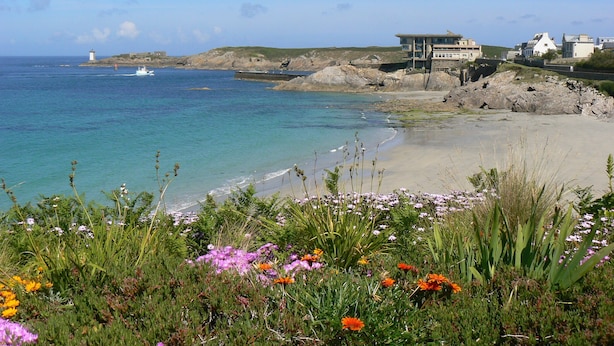 A coastal view with a beach, a lighthouse, and buildings. - The waterfront Maison des Seigneurs (Le Conquet)